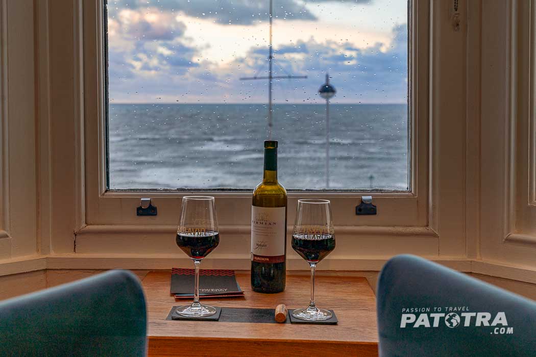 Eine Flasche Wein und zwei Gläser vor dem Fenster mit Ausblick auf das Meer